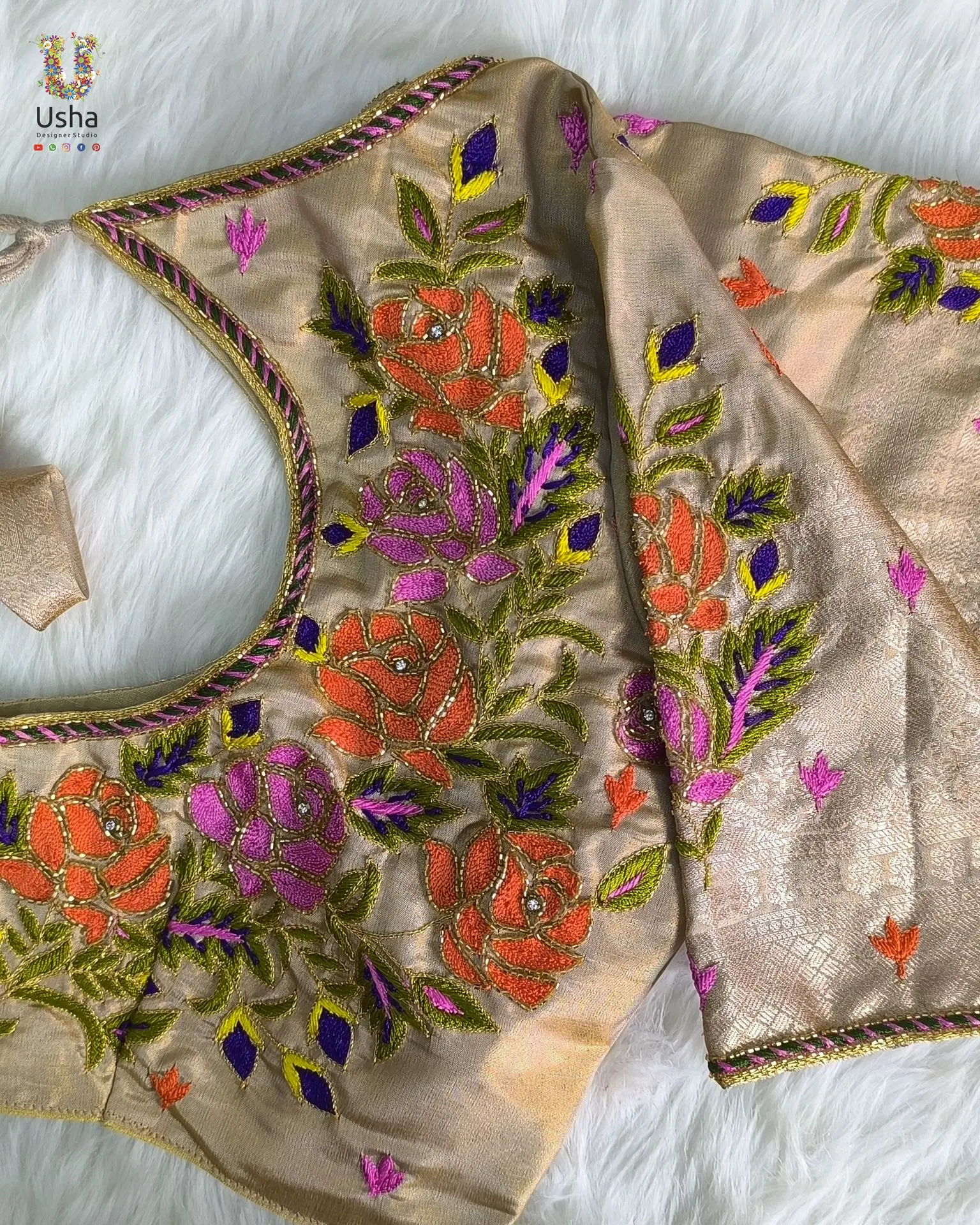 Beige tissue blouse with vibrant floral aari embroidery in orange, pink, and violet, handcrafted by Usha Designer Studio
