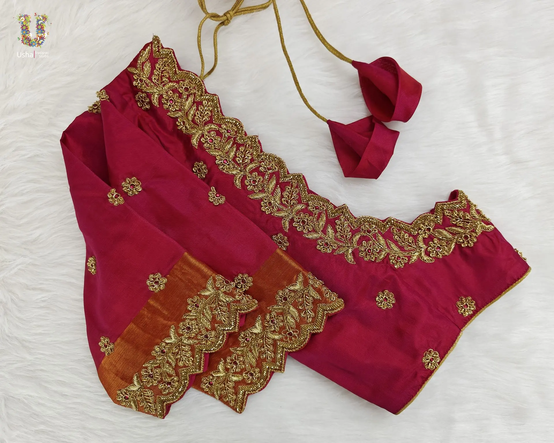 Crimson bridal blouse featuring golden aari embroidery, scalloped neckline, and rust orange zari border, designed by Usha Designer Studio