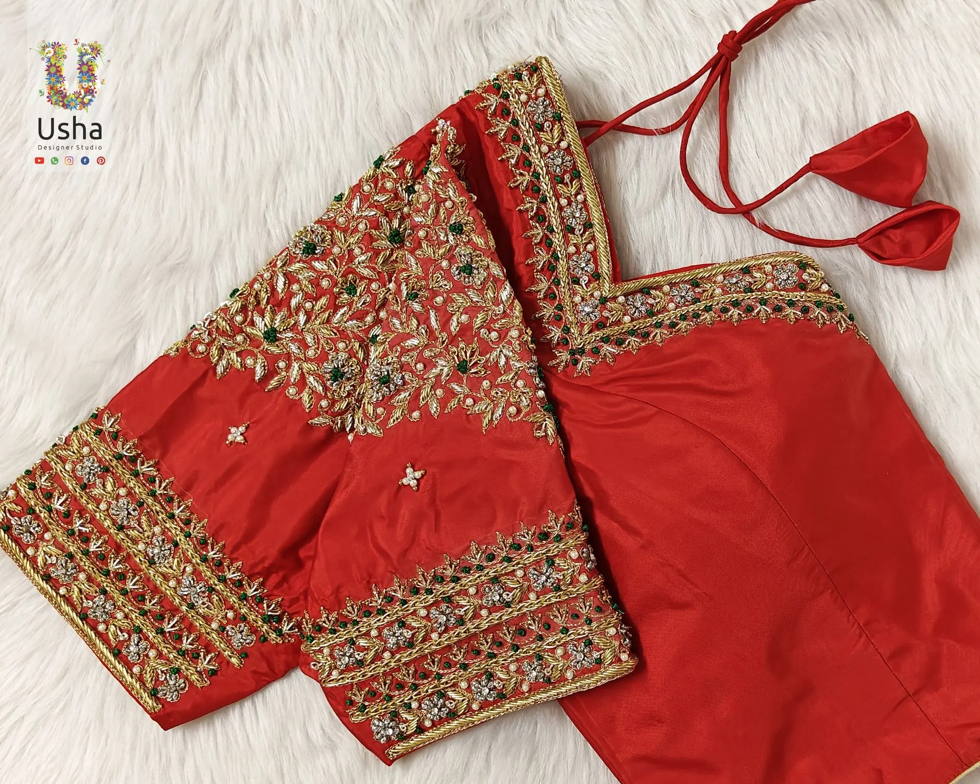 Vibrant red bridal blouse featuring heavy aari and maggam hand embroidery with floral and leaf motifs in gold and green, designed by Usha Designer Studio
