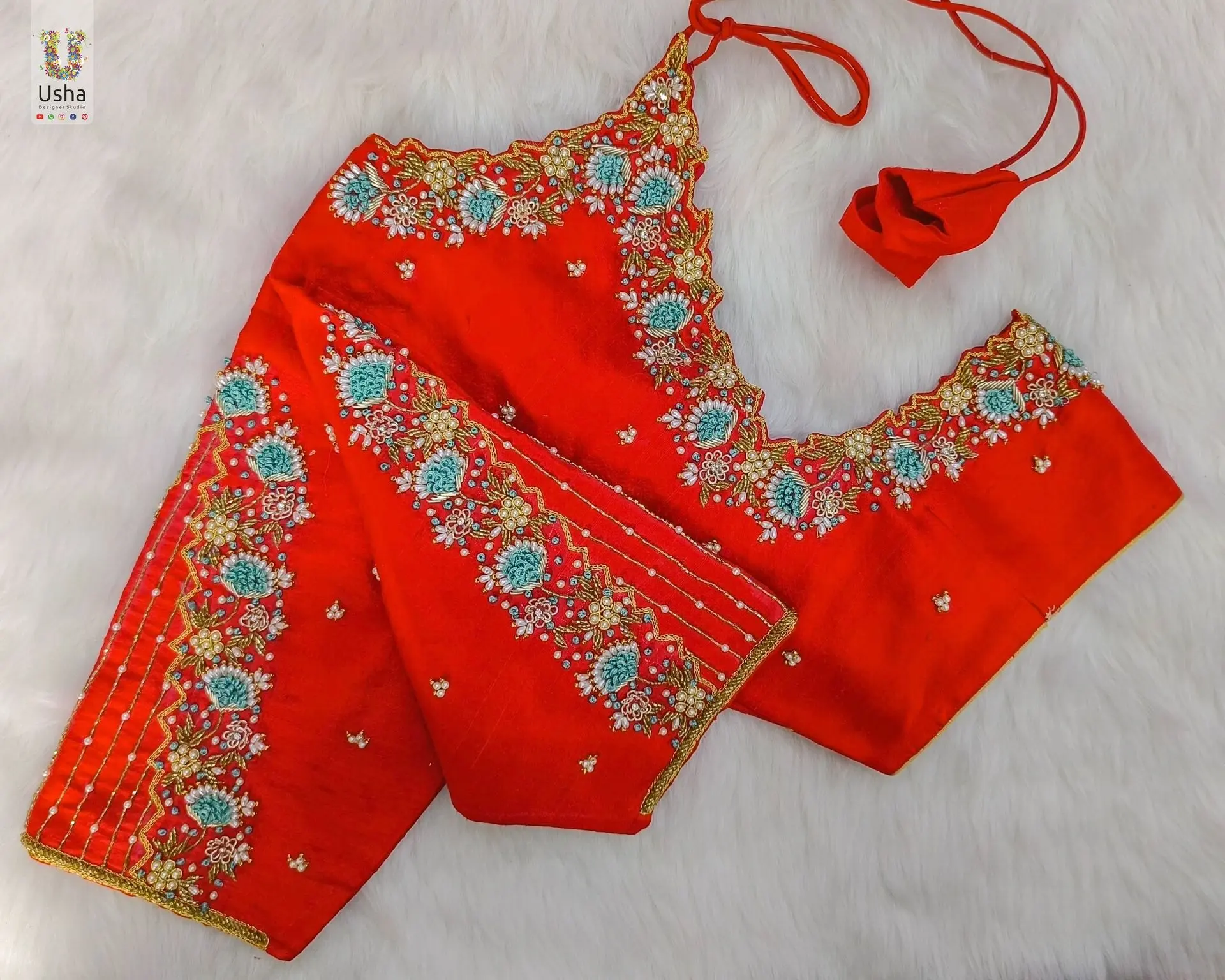Vibrant red bridal blouse featuring heavy aari and maggam hand embroidery with floral and leaf motifs in gold and green, designed by Usha Designer Studio