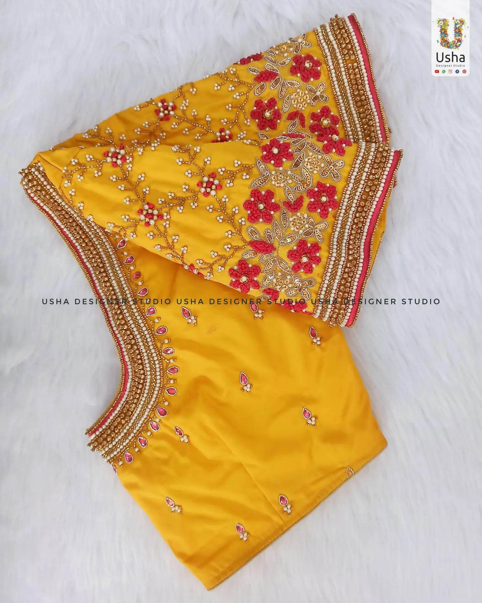 A heavily embroidered mango yellow bridal blouse from Usha Designer Studio. The sleeves are covered in a dense floral pattern of pink, gold, and pearl beadwork, finished with a thick, ornate zardosi border that also details the neckline.