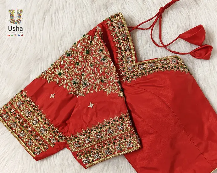 Vibrant red bridal blouse featuring heavy aari and maggam hand embroidery with floral and leaf motifs in gold and green, designed by Usha Designer Studio