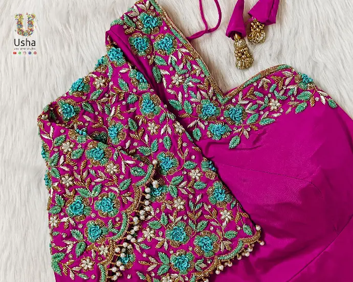 Fuchsia pink bridal blouse adorned with turquoise blue floral aari work, intricate bead detailing, and pearl drops, handcrafted by Usha Designer Studio