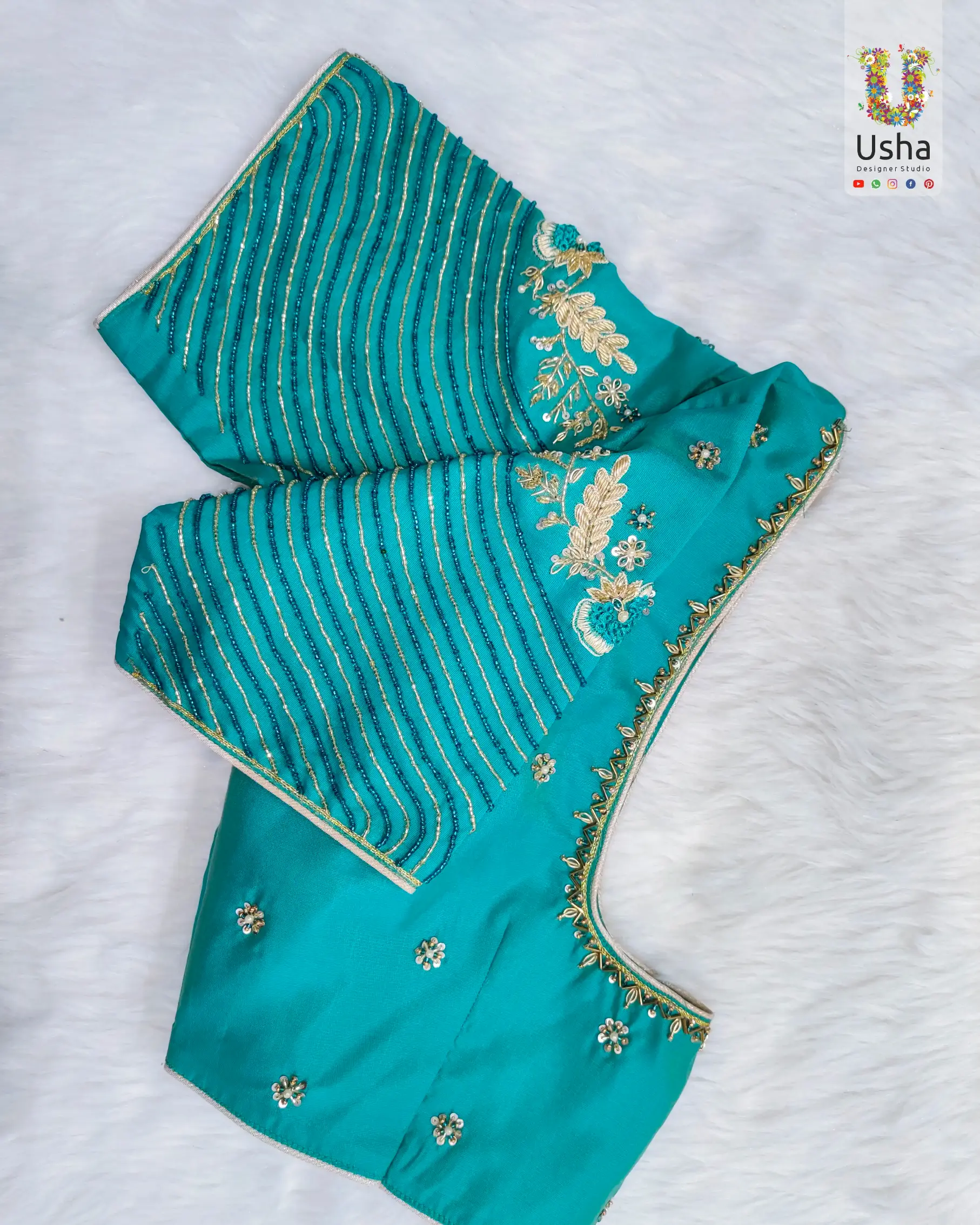 Teal blue designer blouse with intricate Aari embroidery, gold zari floral motifs, and hand embellishments by Usha Designer Studio, Vijayawada.