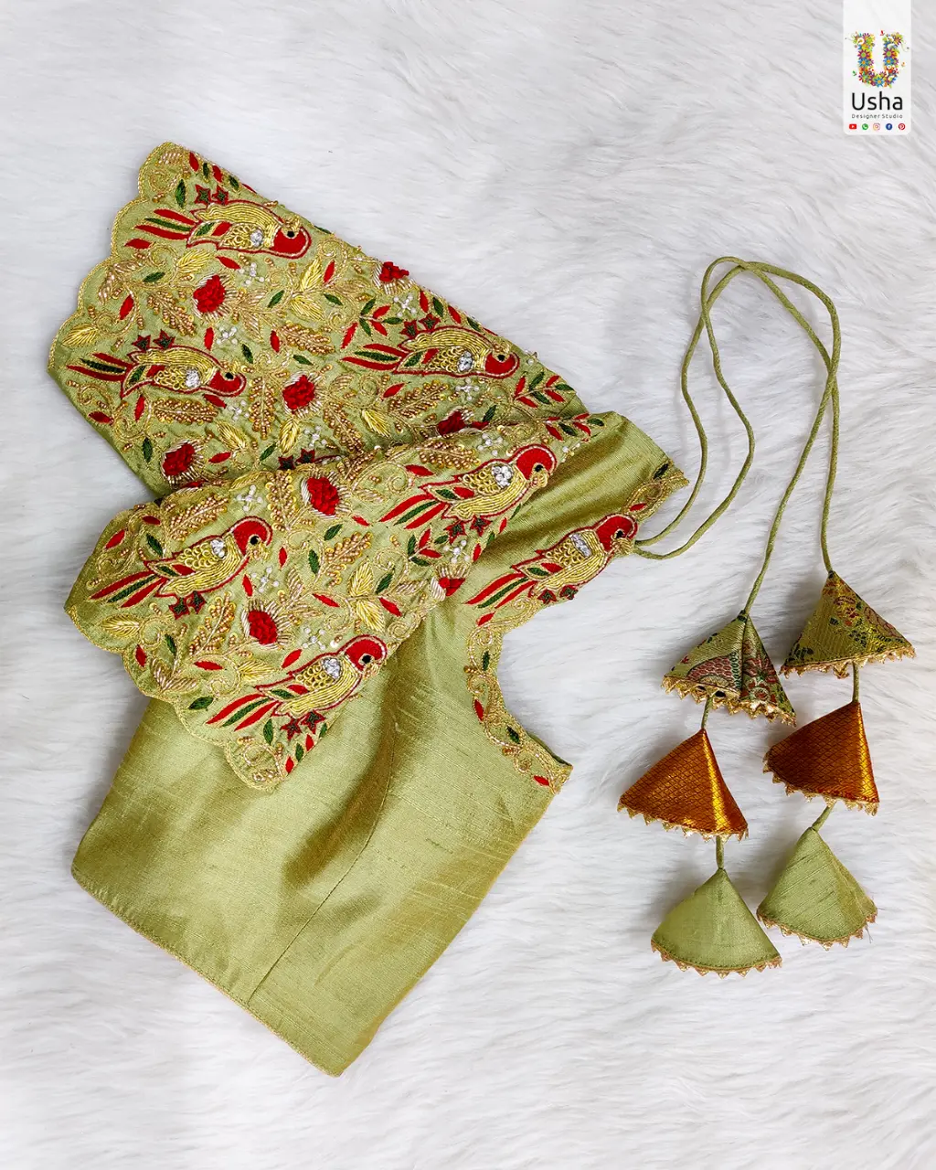 Exquisite Golden-Green Silk Blouse with Intricate Peacock Aari Handwork Close-up of a premium golden-green silk blouse featuring intricate all-over peacock and floral Aari and Zari hand embroidery on the sleeves, with pearl accents and scalloped edges. Includes traditional fabric tassels (latkans) in matching colors.