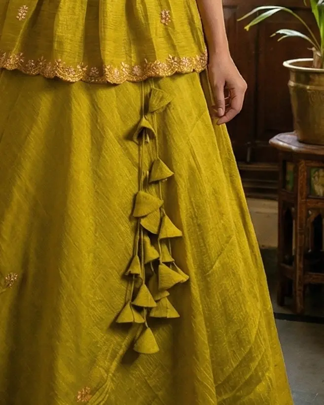 Mustard yellow saree upcycled into V‑neck elbow‑sleeve crop top lehenga with 1‑inch pleated skirt and handcrafted heavy latkans by Usha Designer Studio Vijayawada.