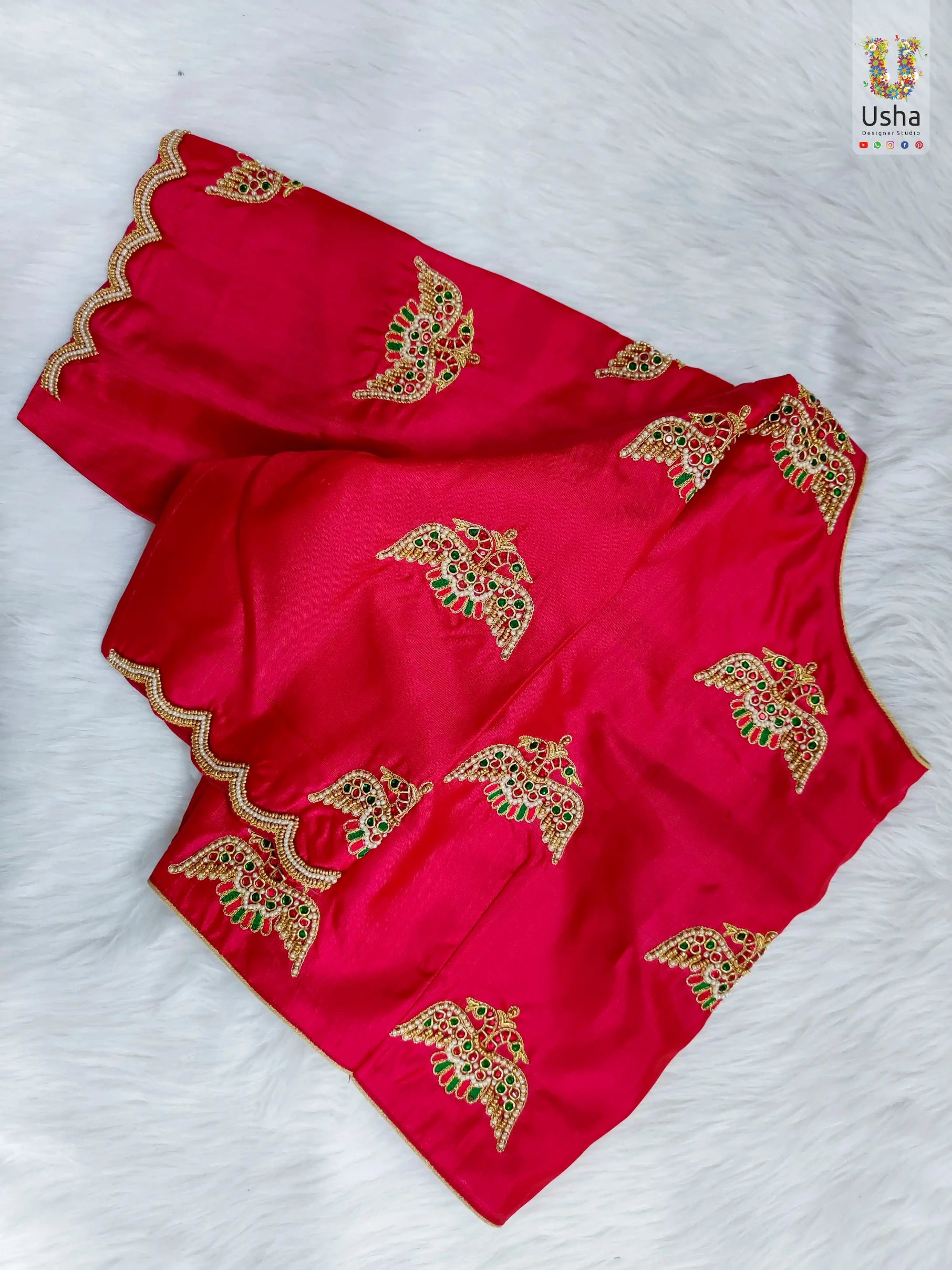 Hand-crafted rani pink silk designer blouse by Usha Designer Studio featuring intricate gold Aari embroidery bird motifs, red and green stone embellishments, and custom scalloped sleeves.
